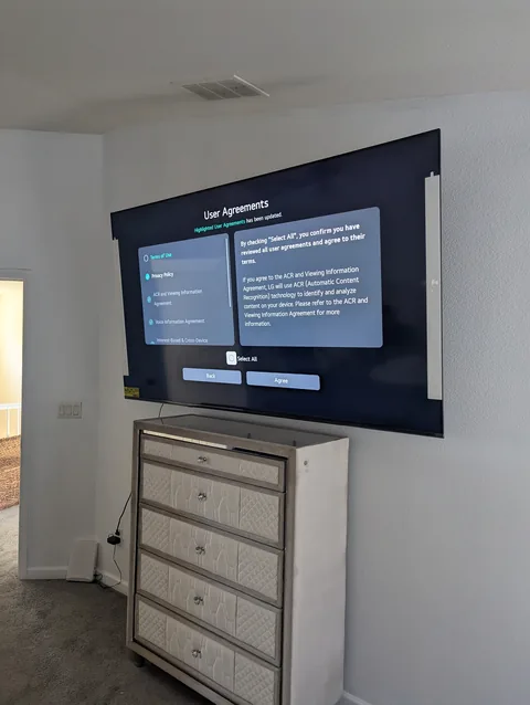 85-inch TV mounted on a bedroom wall above a dresser